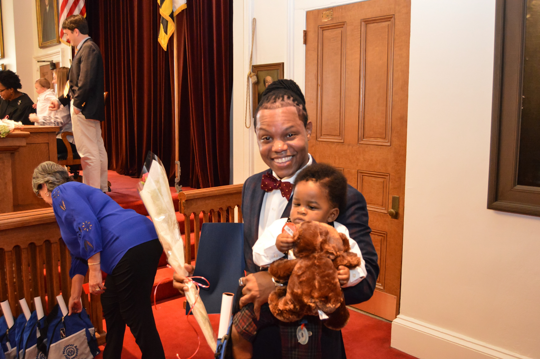 An adult holding a child and a teddy bear in a courtroom